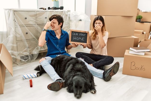 eliminate fart odor, picture of a young couple unpacking the new home setting on the floor with their dog while holding their nose. 